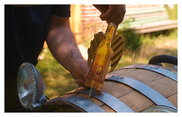 Fassbrause Maracuja wird über Holzfass gehalten