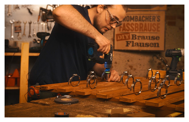 Schlauchschellen werden auf Brettern mit einem Akkuschrauber angebracht.