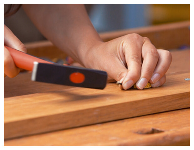 Mit einem Hammer wird ein Nagel in ein Holzbrett geschlagen.