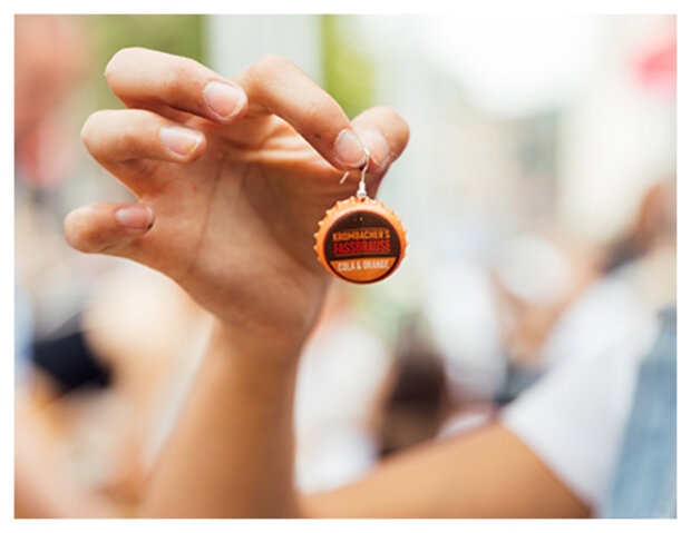 Hand hält Ohrring mit Kronkorken