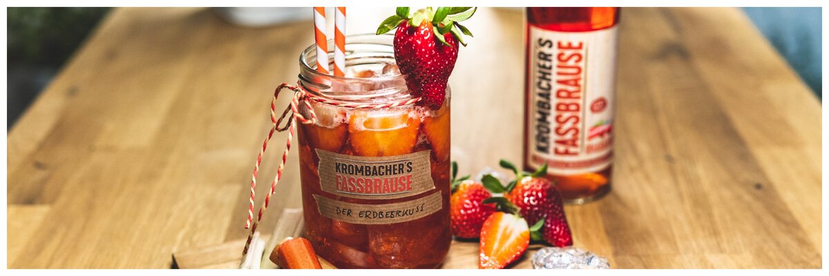 Cocktailglas mit Krombacher Fassbrause Rhabarber angerichtet mit Erdbeeren und Text: Erdbeerkuss