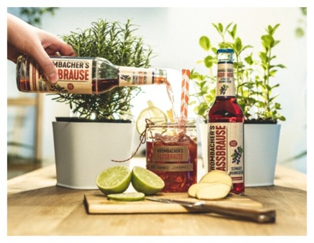 Eine Hand gießt Rothaus Brause in ein Glas mit Limettenscheiben und einem roten Strohhalm. Auf dem Tisch stehen zwei Flaschen Rothaus Brause und zwei Pflanzen in Töpfen.