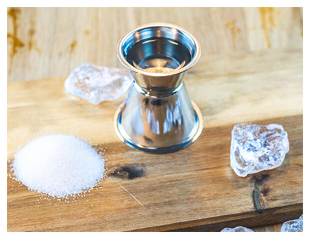 Zuckersirup in Behälter mit Zuckerhäufchen daneben.