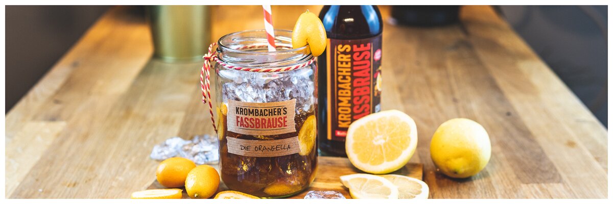 Cocktail mit Krombacher Fassbrause Cola-Orange und Eiswürfeln und Text: Orangella